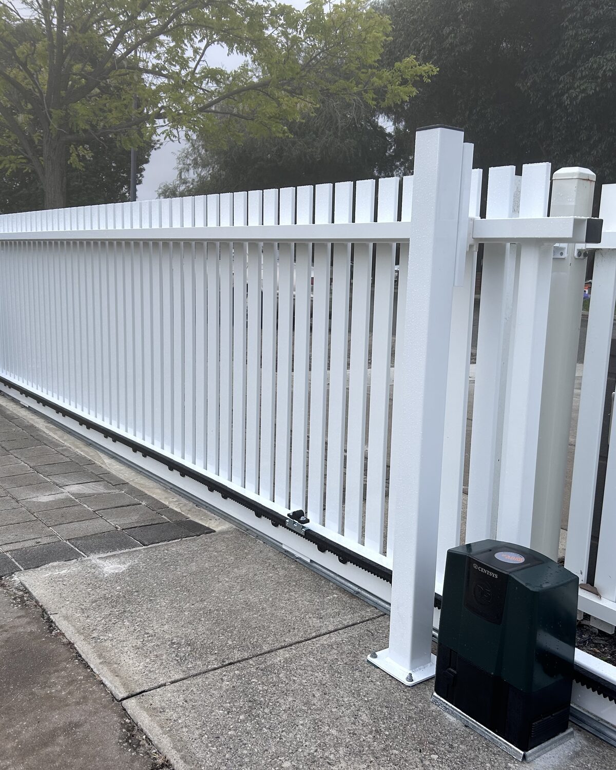 Sliding gate motor and rack beside a white gate